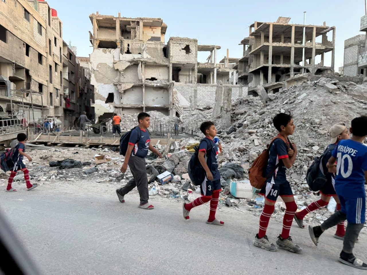 Children in sports kit walking to school past damaged buildings